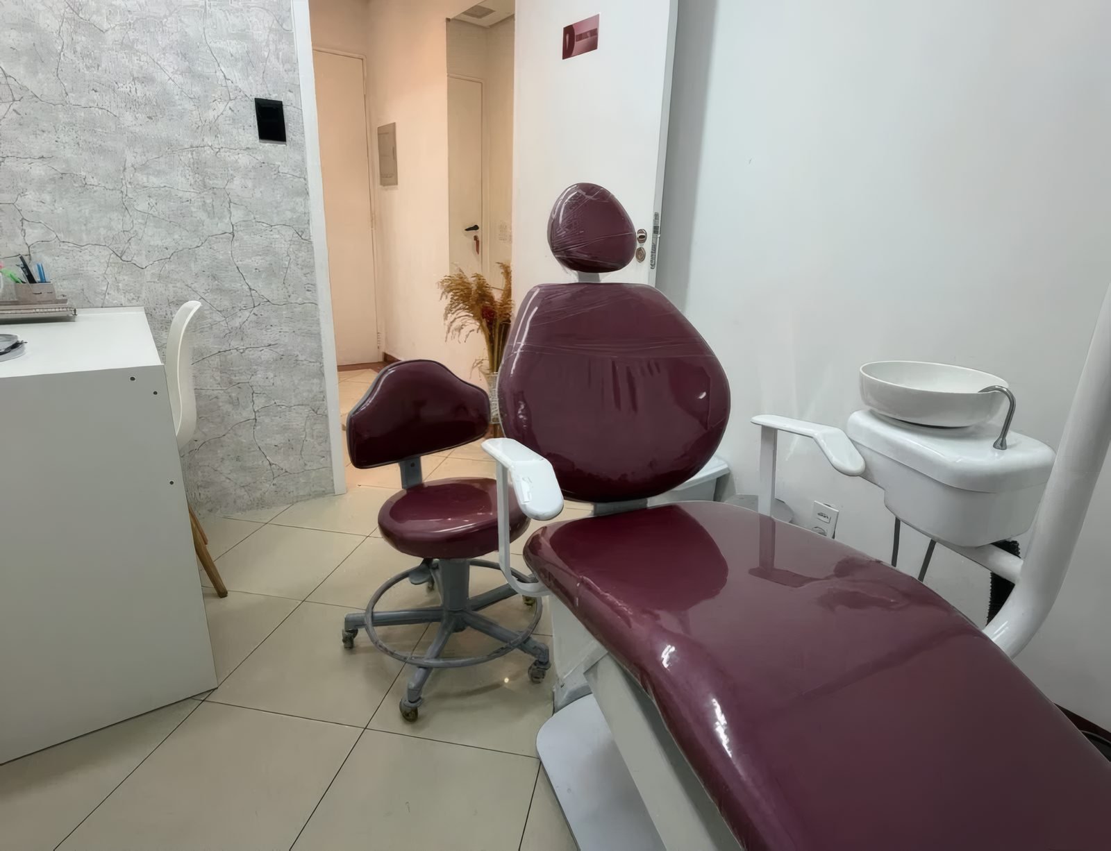 Sala de atendimento com cadeira odontológica vinho e mocho
