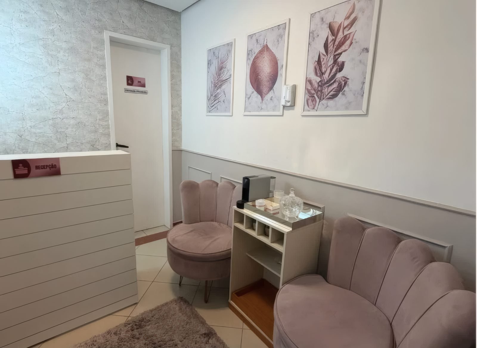 Sala de espera com poltronas rosé, quadros de folhas e cantinho do café